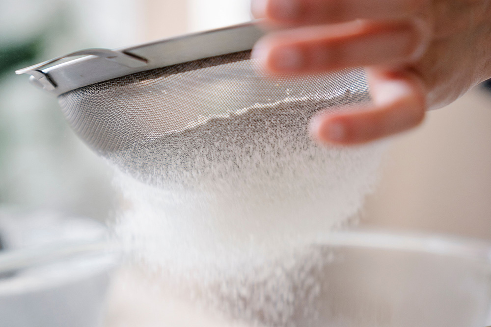 Flour is sifted into a measured bowl to suggest the process of measuring and making consistent a work in book editing