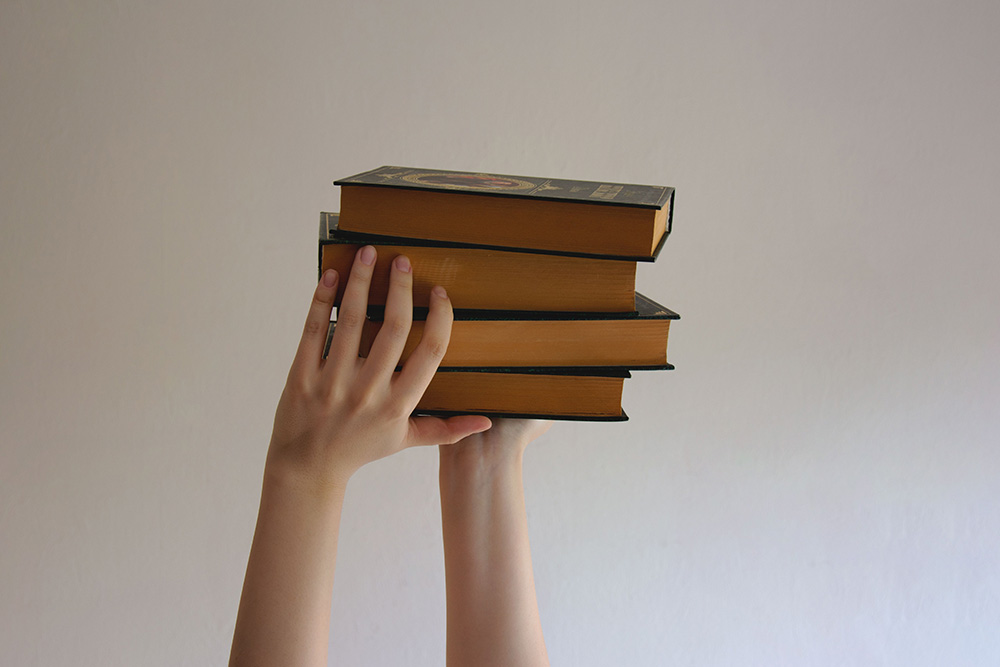 Four books are sat up in hand together and all look similar to another to suggest the four stages of editing the same book, a parallel for book editing