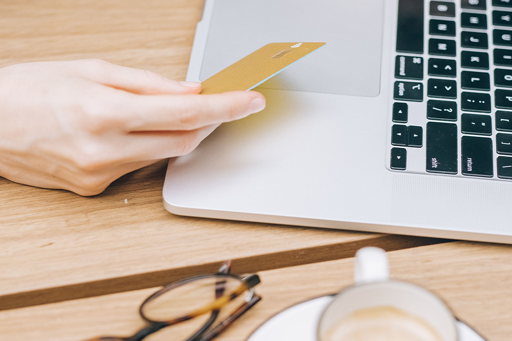 A hand with credit card in-hand and a laptop open suggests spending on amazon marketing services in a light and positive tone armed with the information of this article