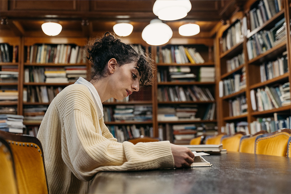 A woman seemingly captivated by a book in a library to suggest when you might want to use contractions in writing
