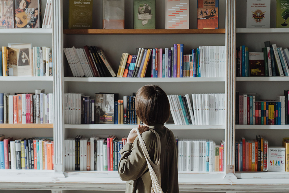 A woman sits stands affront a bookcase sort of dreaming to suggest that it's not unrealistic to ask how much does it cost to publish a book?