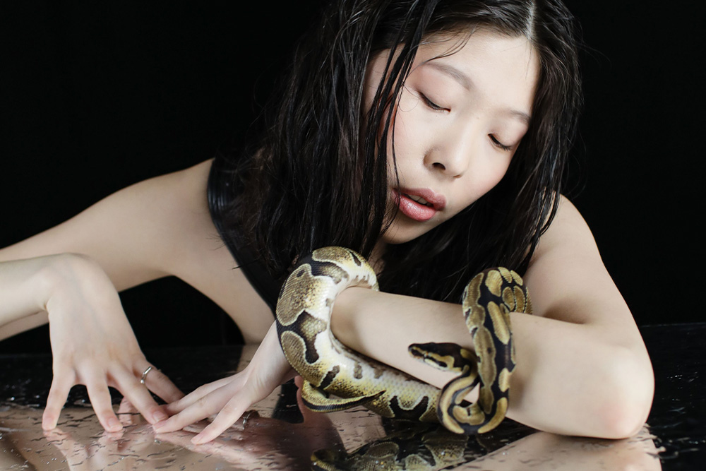 A woman stares adoringly at a snake wrapped around her arm to suggests that the reader naturally follows a danger present in the story when the main character is the villain 
