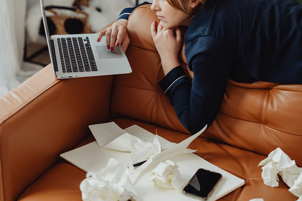 A picture of a woman working on a laptop with balled up pieces of napkins and tissues beside her as a parallel for mistakes in how to write an author bio
