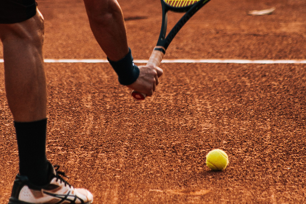 A tennis ball on a clay court about to be picked up