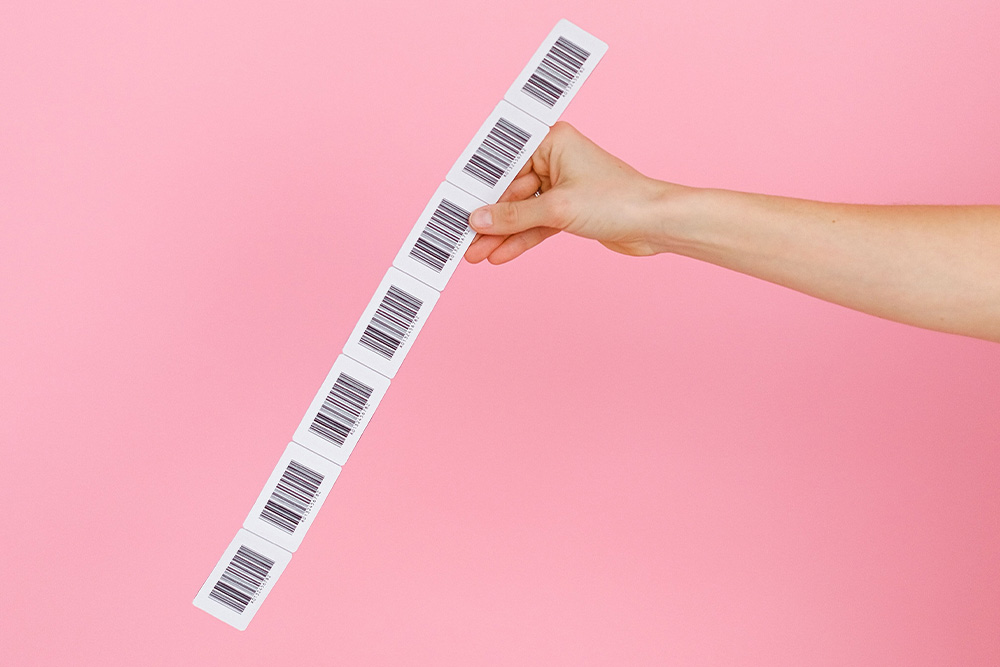Barcodes held up by a hand against a pink backdrop to suggest the connection to how to get an isbn for your book