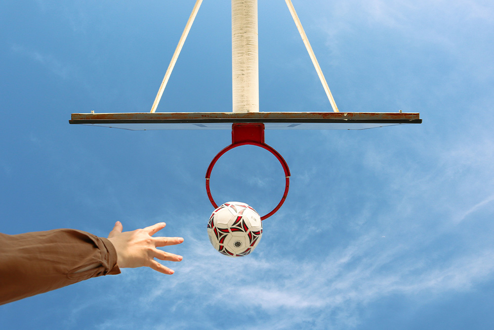 A hand throwing a soccer ball into a basketball hoop to suggest many issues with goals that are improperly measured in making proper meaning for personal growth