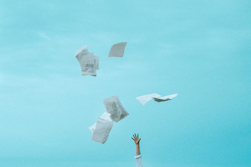 A hand reaching out toward pages spilling into the air suggests a distance from the work that is mended by personal growth