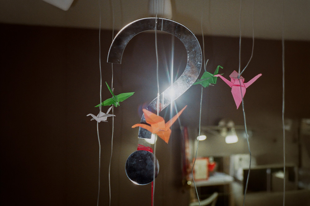 A question hangs from the ceiling with origami birds next to it as a pretty denotation of the dramatic question