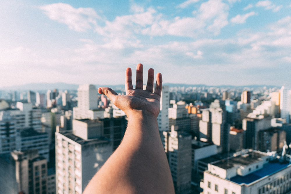 A first person omniscient perspective image of a hand reaching over a city