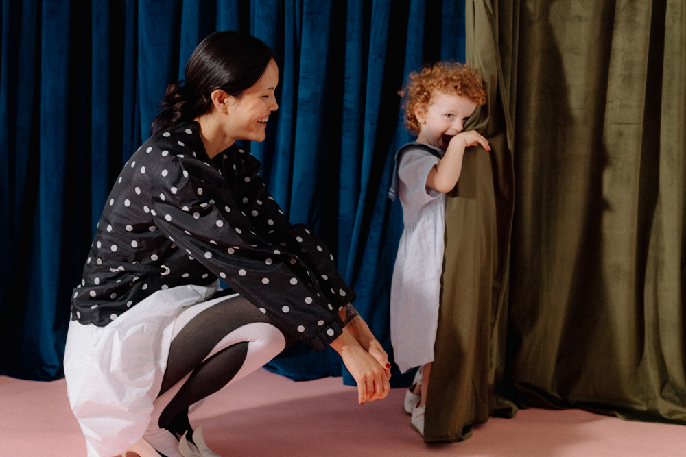Death to Stock - A woman next to a child by a curtain, suggesting a kind of play in reinventing fantasy tropes