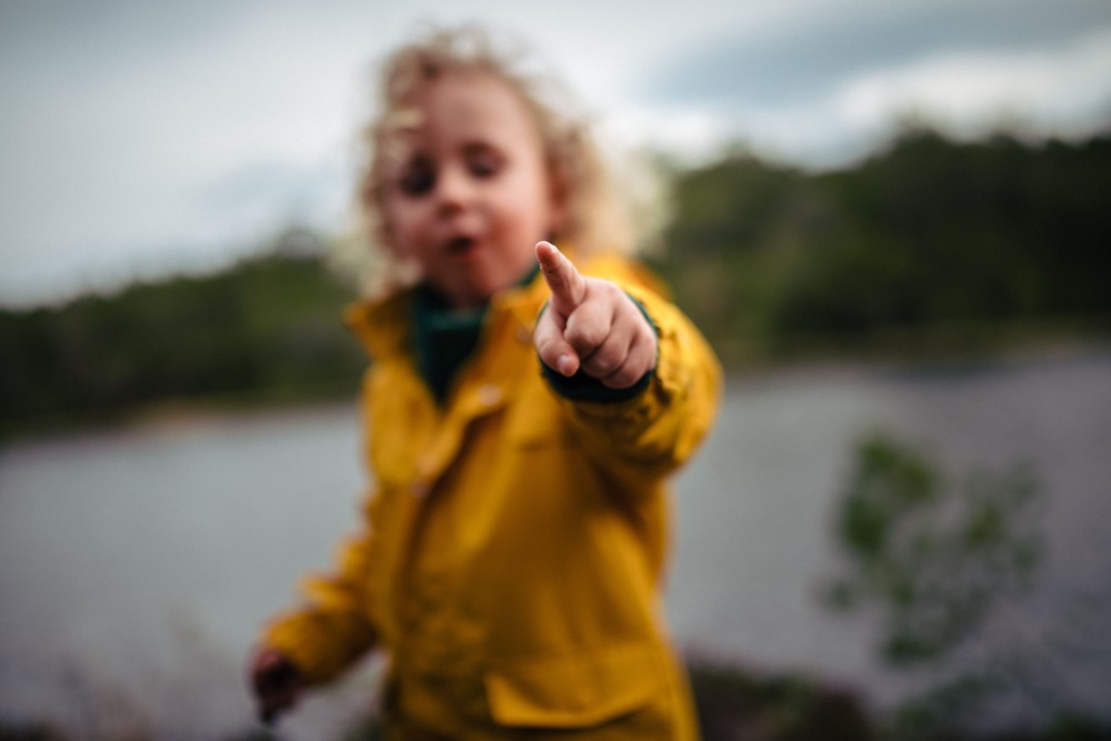 A child in a yellow raincoat pointing at the camera to show the second person point of view in literature.